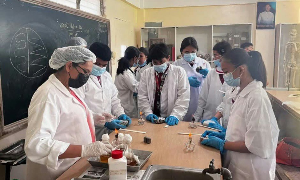 LJNHS Grade 8 STE students in lab coats work on microbial preparation with CPAC Biology faculty at a laboratory bench